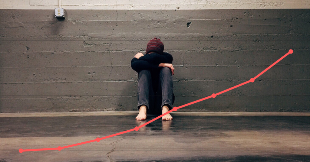 A teenager sitting against a wall with their head in their lap. A red graph going up is laid over the image.