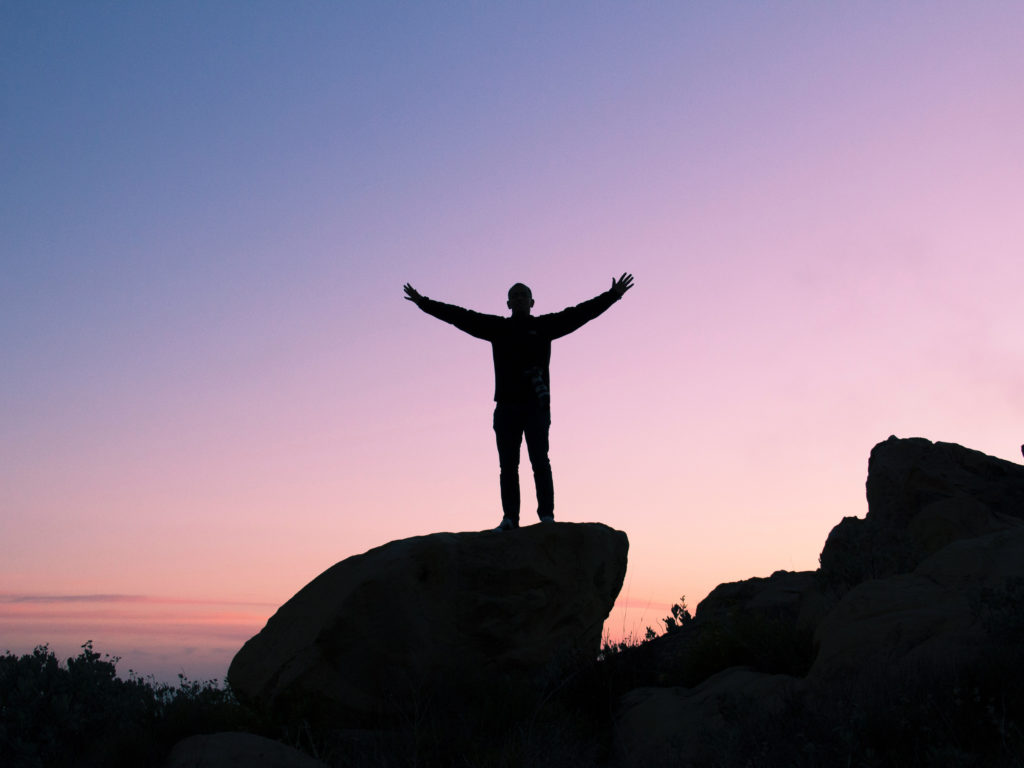 A silhouette of a young man standing on a rock in the desert at sunset.