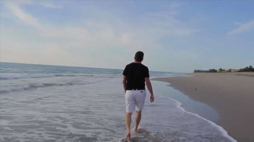 Wide shot of a middle-aged man walking away from the camera on the beach.