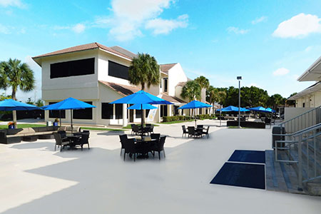 A view of the outside seating area at Beach House Recovery center with tables and blue umbrellas.