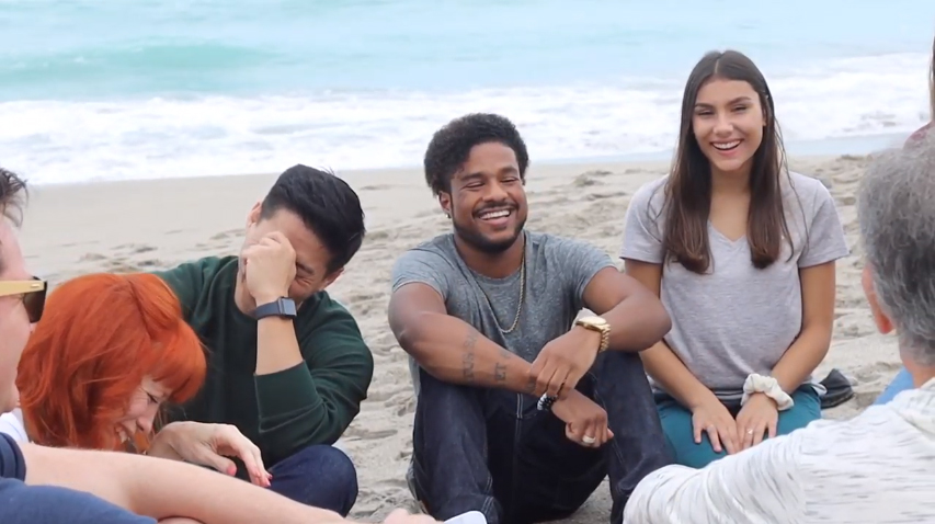 Smiling group of men and women taking part in a group therapy session on the beach.