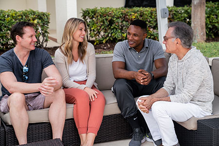 A group of men and women smiling during a therapy session outside.