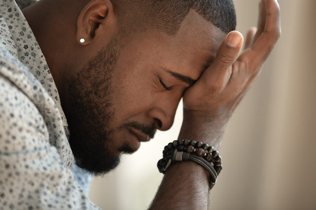 A african-american man holding his forehead. He appears distressed or in pain.