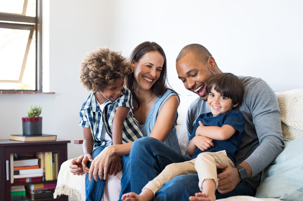 A family smiling and playing together on the couch.