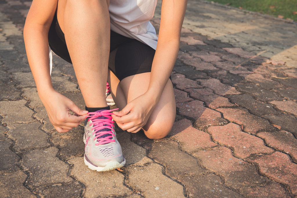 A close up of a young caucasian woman kneeling down to tie her shoelaces before going for a run.