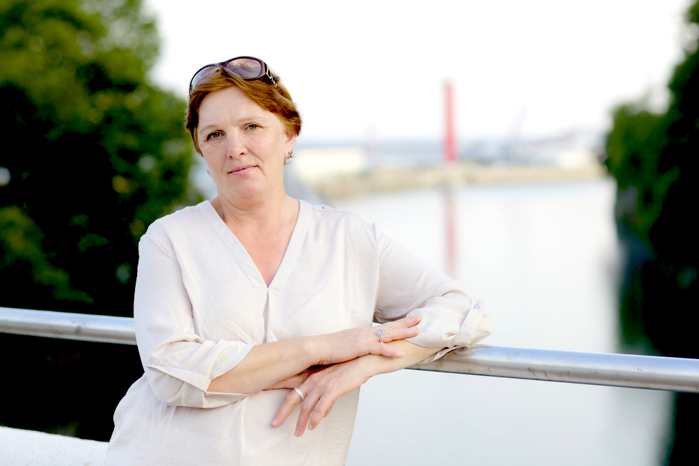 Portrait of an adult woman standing in a park with a river in the background.