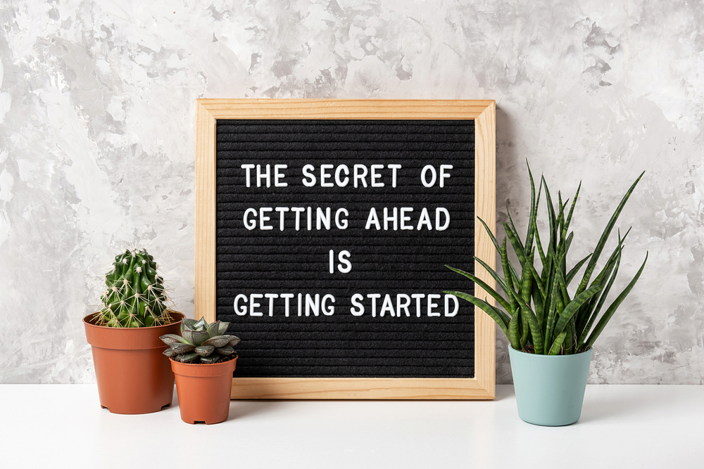 A letterboard surrounded by plants with the message 'The secret of getting ahead is getting started'.
