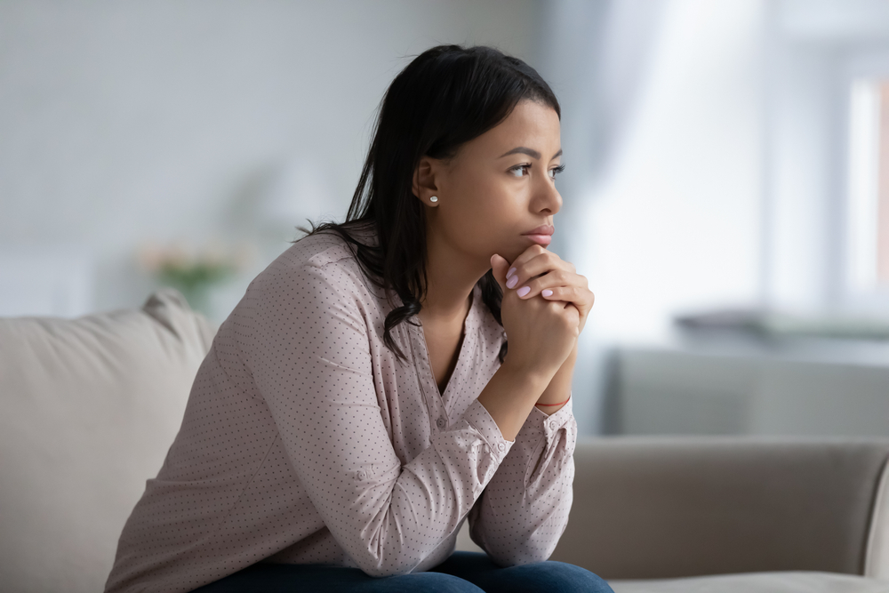 African-american woman sitting on a couch looking troubled.