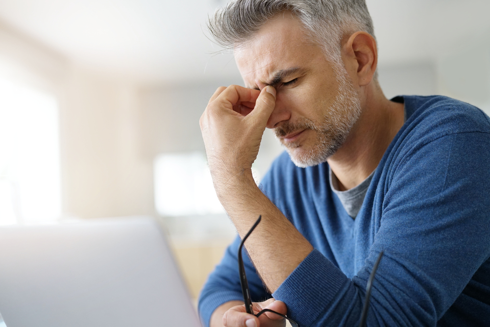 Older male sitting at his desk with his head in his hands.