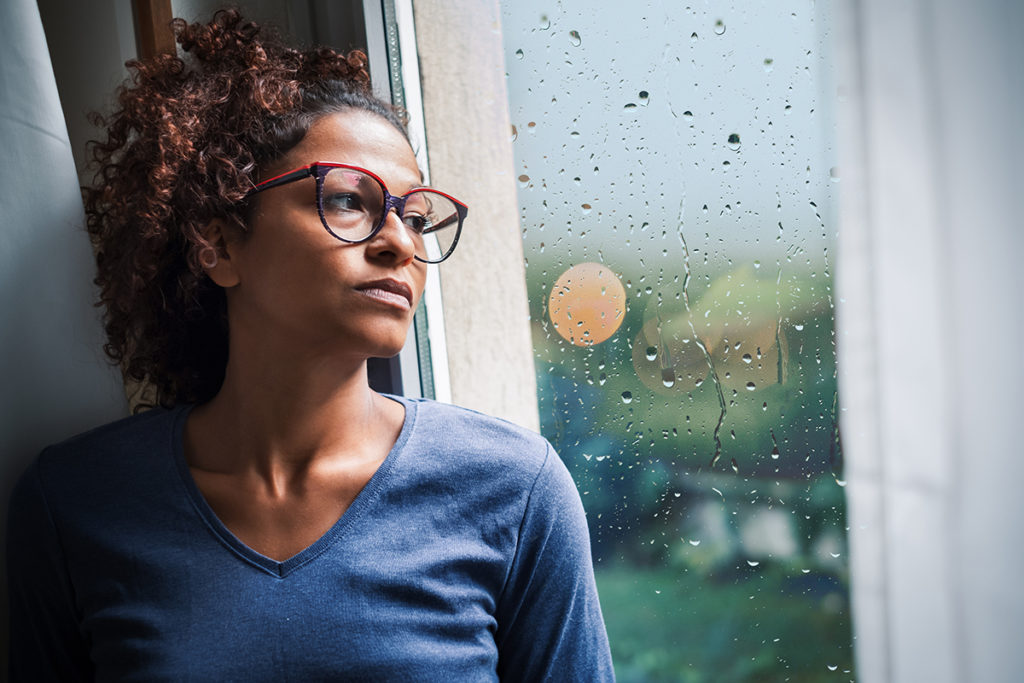 An african-american woman looking out a window looking pensively at the rain