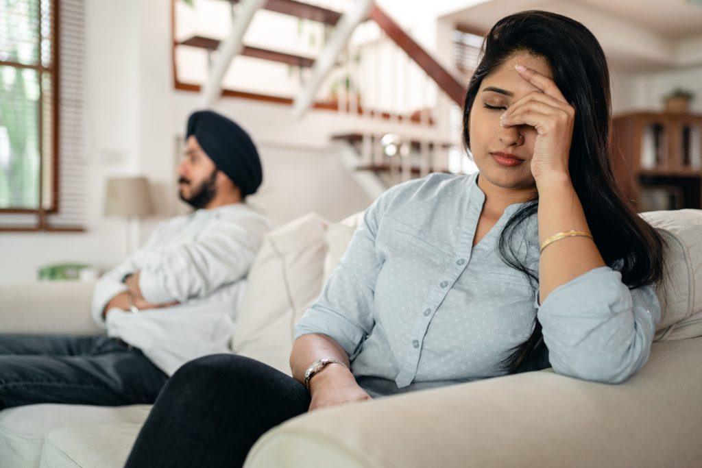 An indian couple sitting on a couch. They appear to have had an argument.