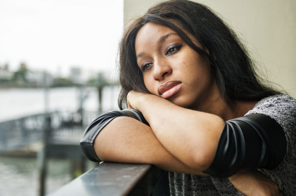 An african-american woman sitting with her head on her arms looking sad.