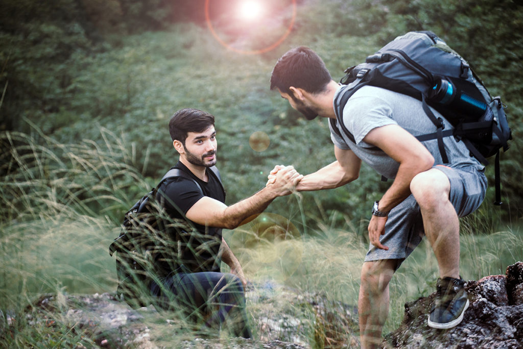 Two caucasian men hiking and helping each other climb over rocks.