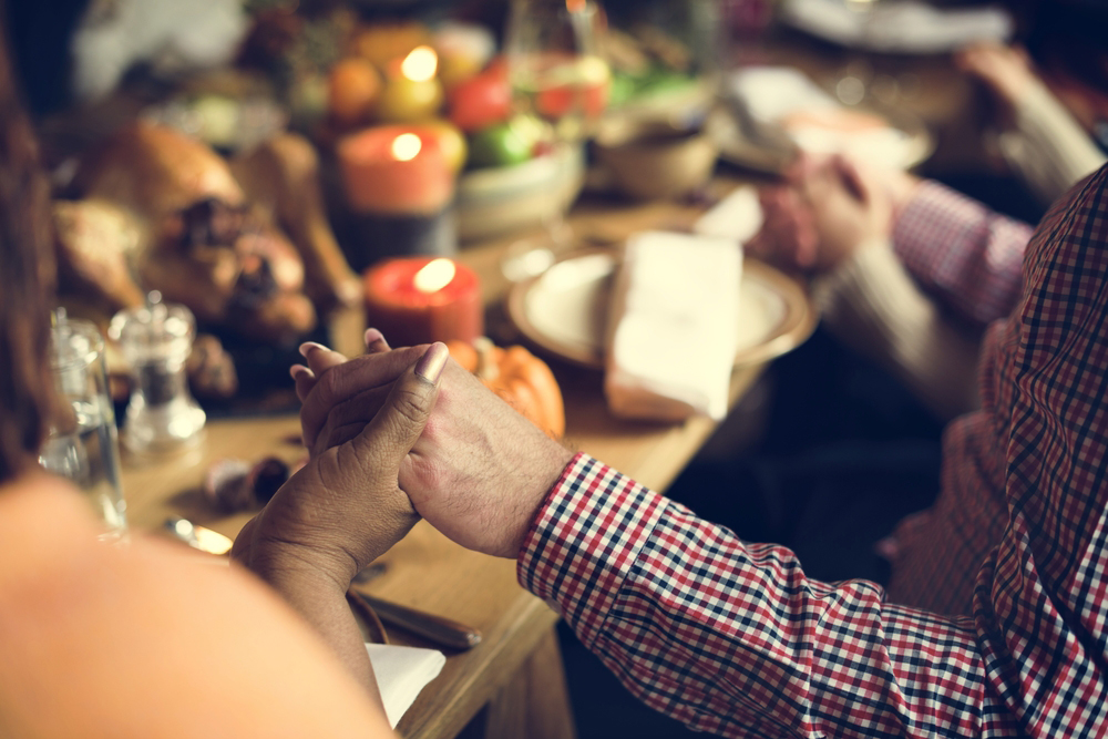 A close up of people holding hands in prayer around a festive dinner table