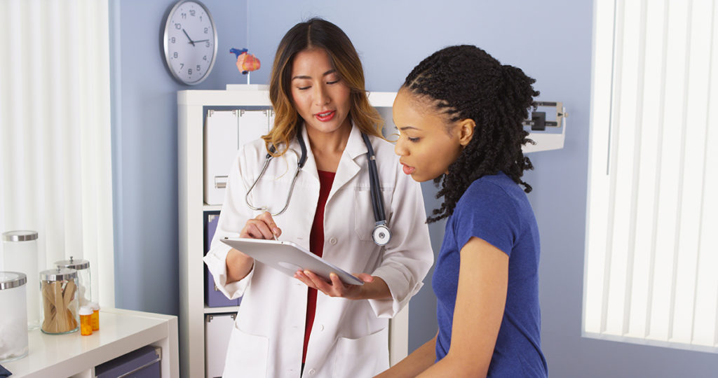 An asian female doctor discussing results with her african-american female patient.