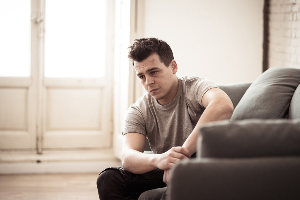 Caucasian male sitting on the couch looking worried.