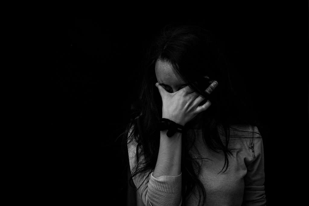A black and white portrait of a young woman crying with her head in her hands.