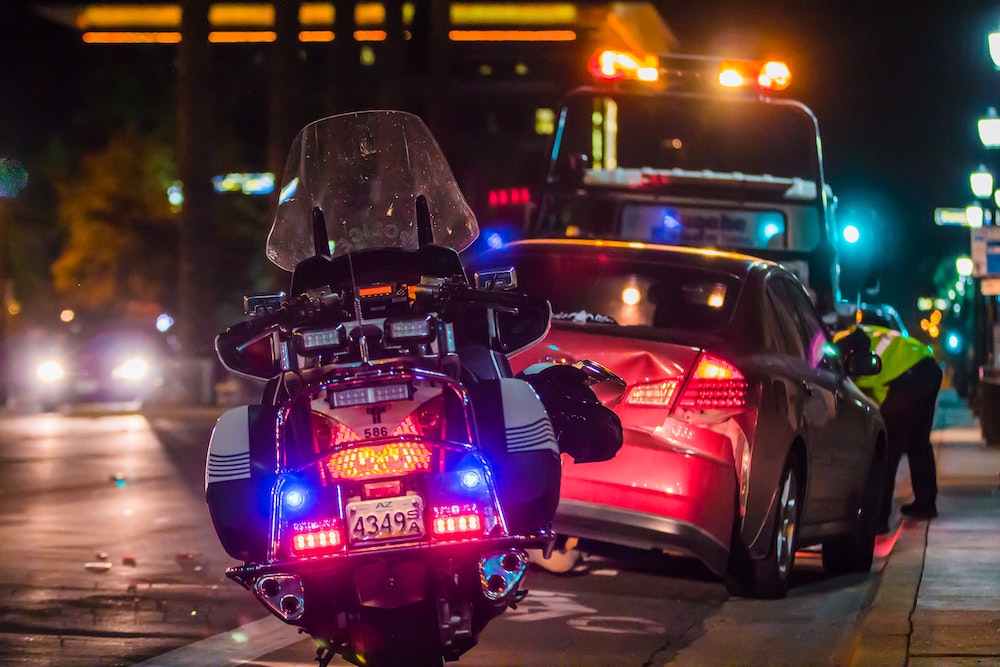 Scene of an accident. A police officer bike is in the forefront and a red car is in the background.