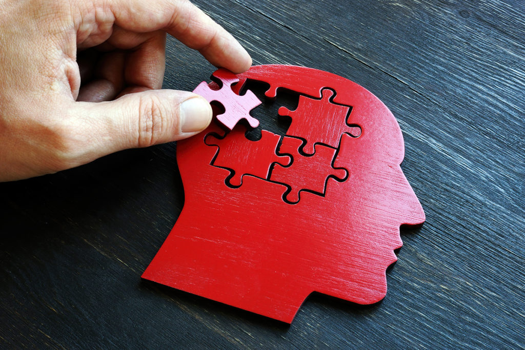A man placing a puzzle piece into a red head shaped puzzle.