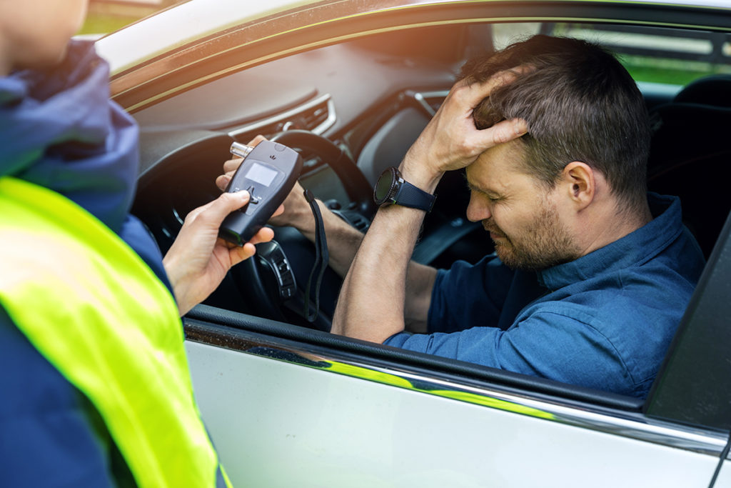 A caucasian male failing a breathalyzer after being stopped by an officer.