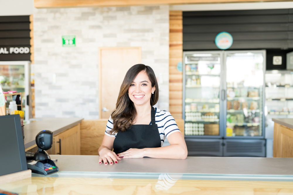 A smiling young woman behind the till of a store.