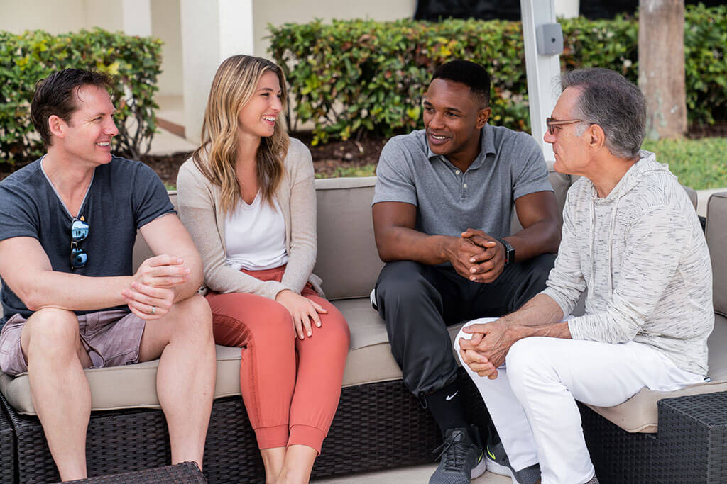 A group of men and women smiling during a therapy session outside.