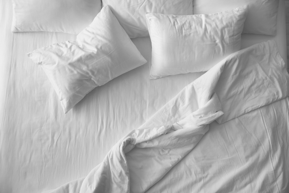 A top view of a unmade bed with white linen.