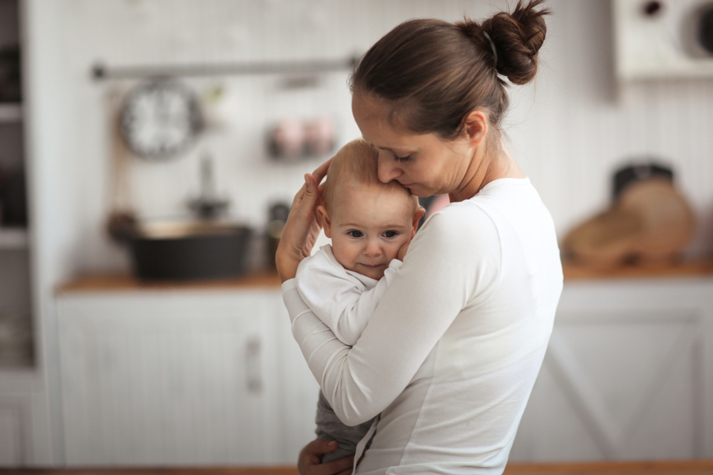 A caucasian mother holding her baby with a kitchen in the background