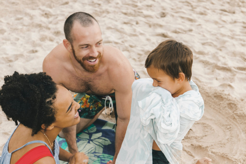 A caucasian father and african-american mother smiling at their son on the beach.