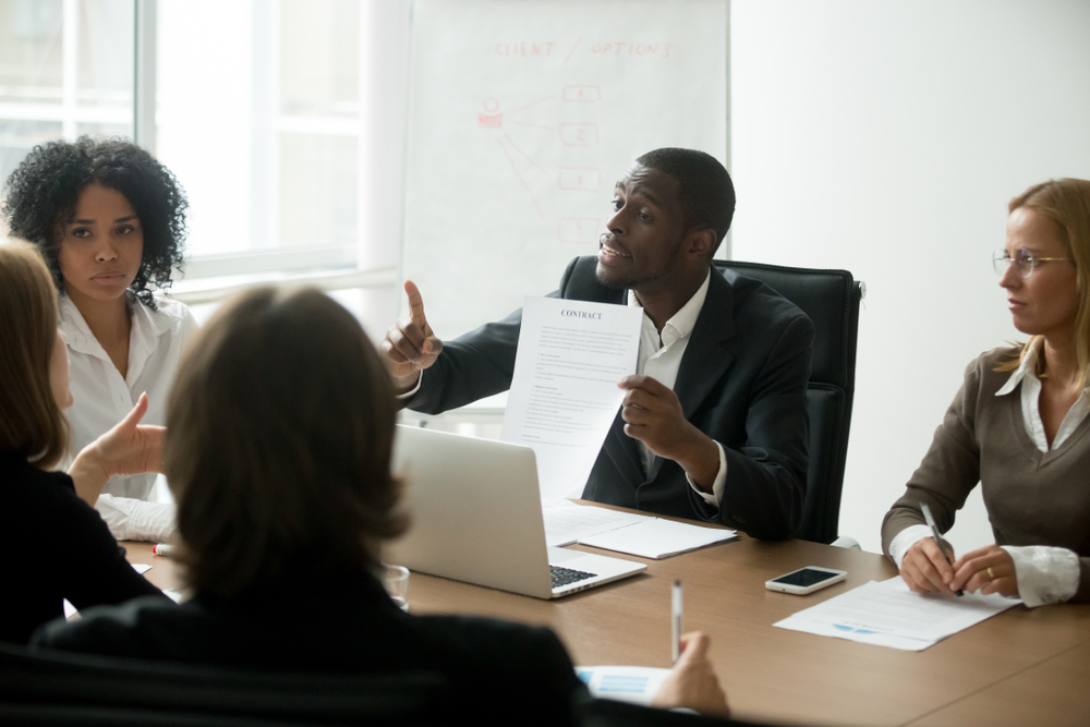 A group of men and women having a business meeting. One africa-american man is holding up a contract while talking.