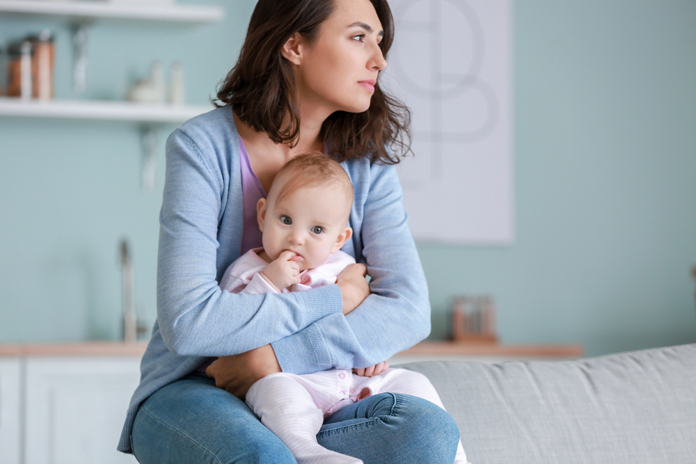 A caucasian woman holding a baby girl on her lap while looking away pensively.