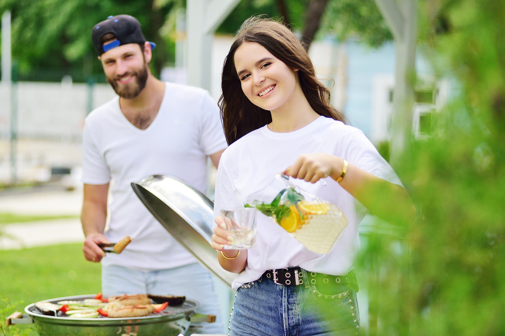 A smiling caucasian man and woman barbequing in the garden.