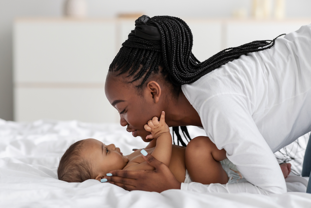 An african-american mother playing with her baby on the bed