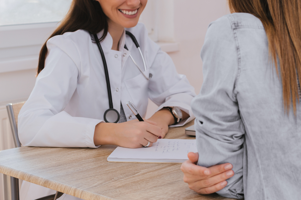 A smiling female doctor taking notes while talking to a female patient