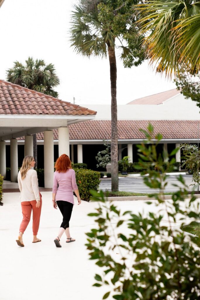 Two caucasian women walking in the gardens at Beach House Recovery Center