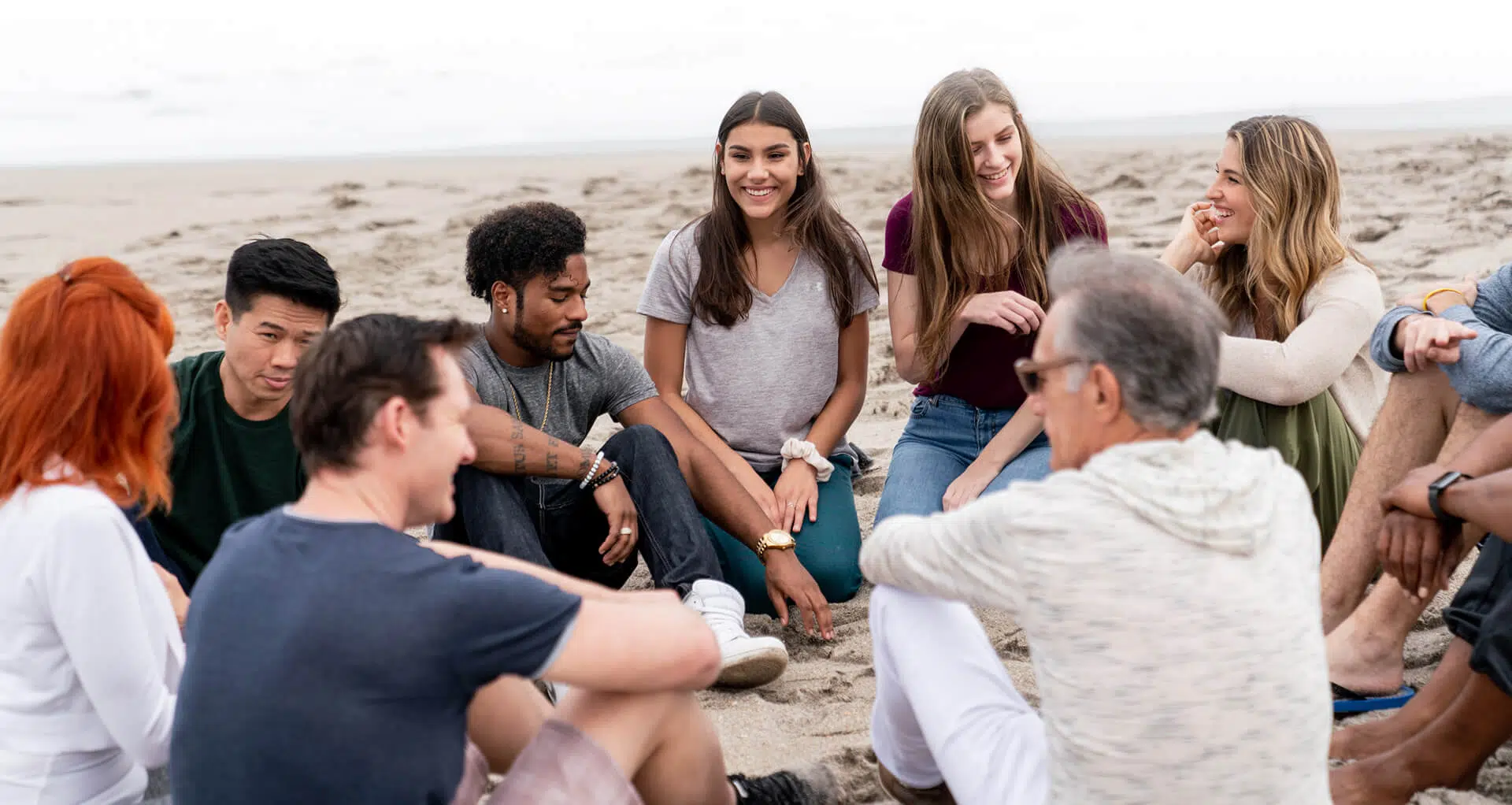 Smiling men and women taking part in a group therapy session on the beach.