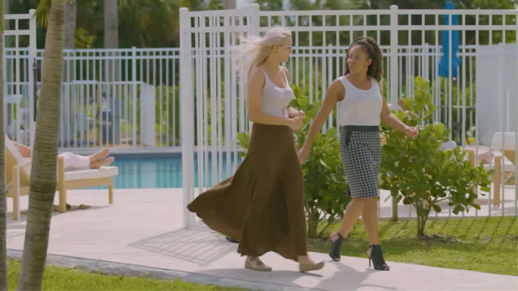 Two women in white, strolling by pool