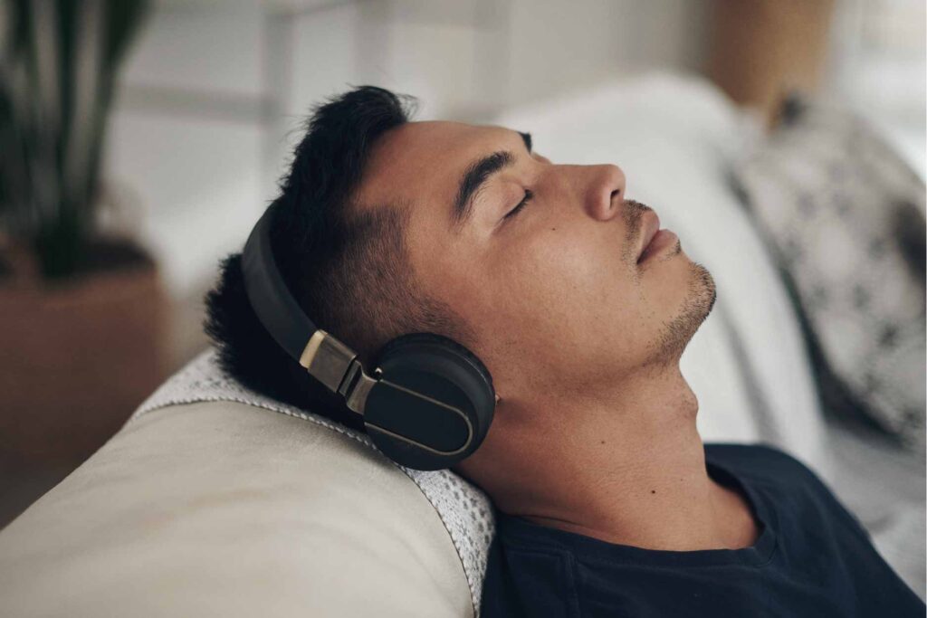Man with headphones on laying down with his eyes closed