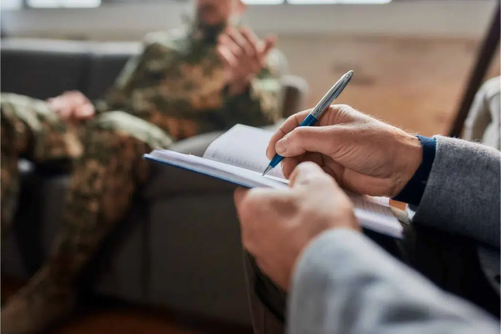 Close up of therapist taking notes while talking to a man in camos