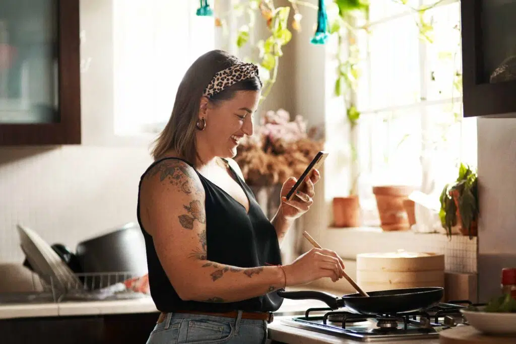 Happy woman cooking while looking at a recipe on her phone