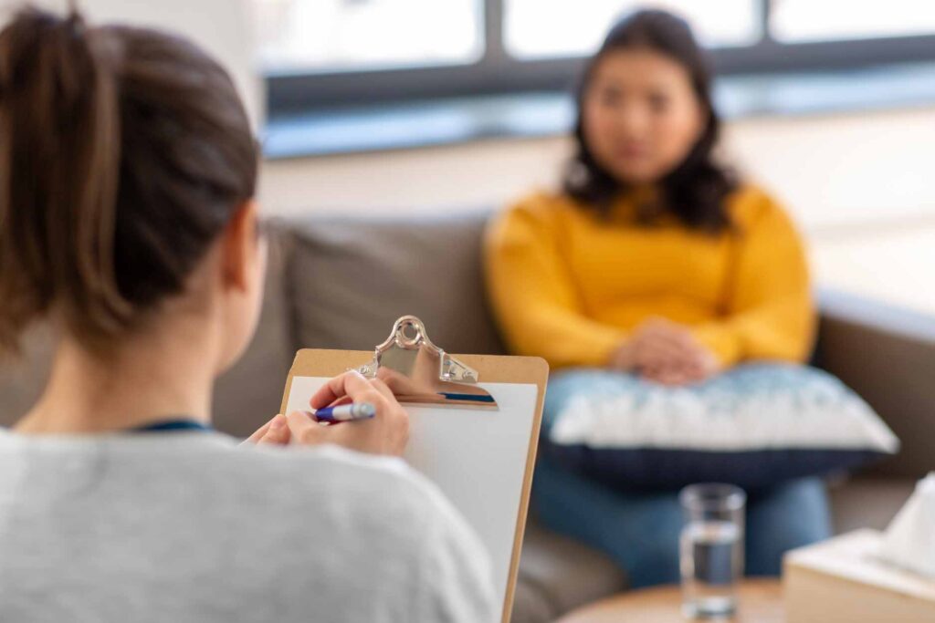 Woman writing on a clipboard while another woman sits on a couch