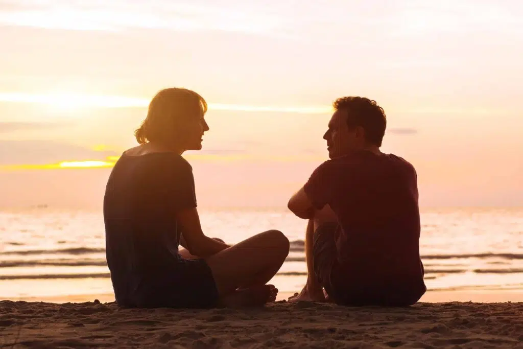 Two people speaking on the beach as the sun sets