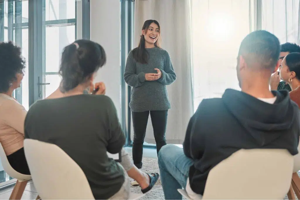 Young woman speaking in front of a group of people seated in a circle