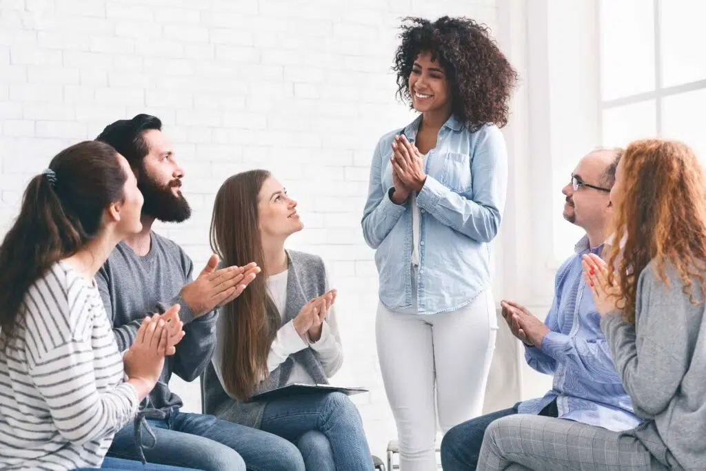 Smiling woman speaking with a group of people clapping for her
