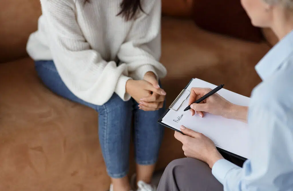 Close up of woman taking notes while a woman sits on the couch