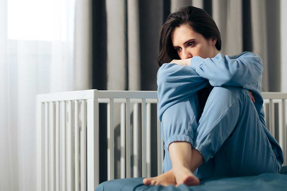 Sad woman sitting next to crib