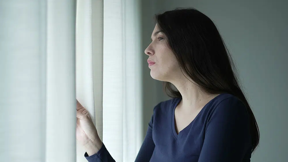 Woman looking out window behind curtain