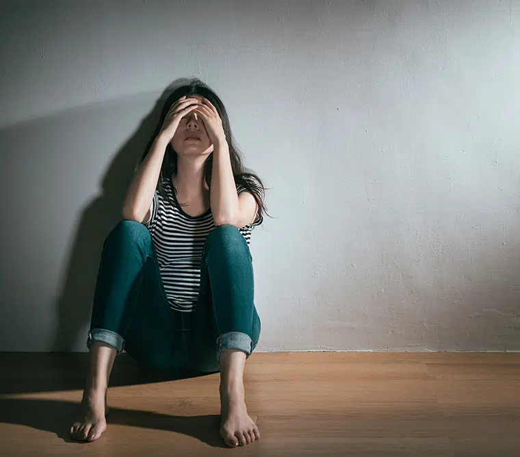 Sad young woman sitting on floor holding head