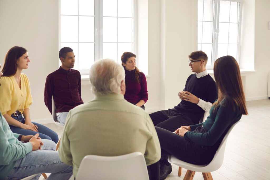 A multicultural group engaged in a therapy group, highlighting the importance of community and shared experiences in the recovery process.