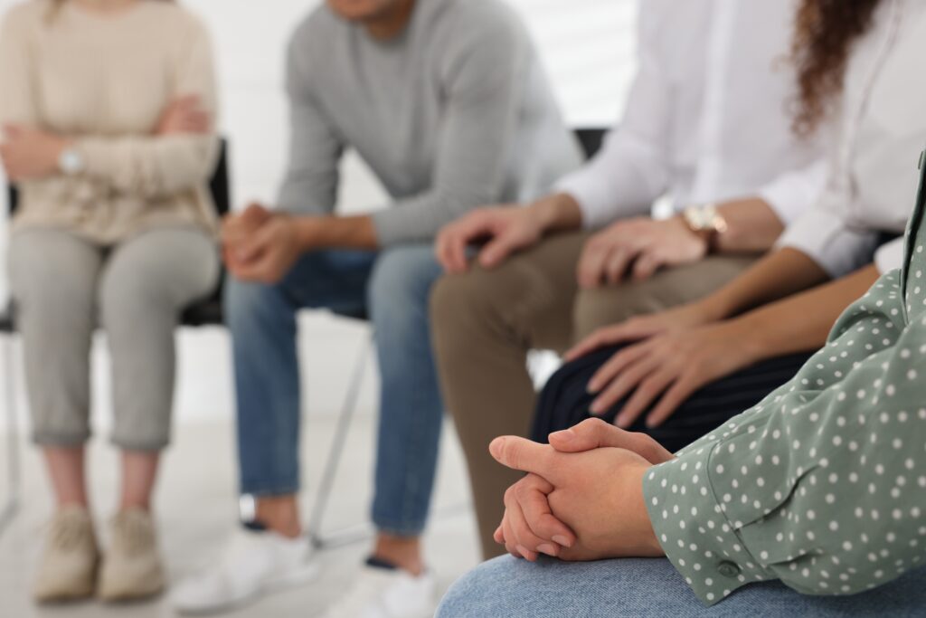 A closeup image of people sitting in a circle at a group therapy session.